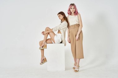 İki kız arkadaş yan yana durur. Moda cazibesi pozu verir.