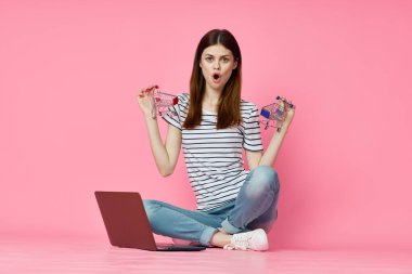 Dizüstü bilgisayarı olan bir kadın internet alışverişinde pembe arka planda oturuyor.