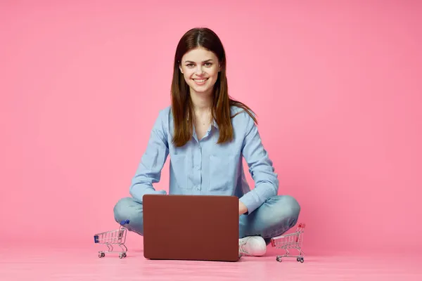 Mujer sentada en el suelo con ordenador portátil compras entretenimiento rosa fondo — Foto de Stock