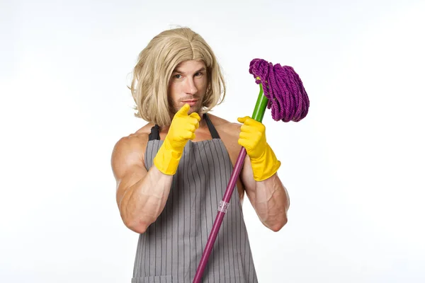 Muscular man in apron with a mop in a womans wig — Stock Photo, Image