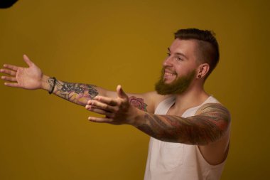 Beyaz tişörtlü maço adam kollarında dövmeler var.