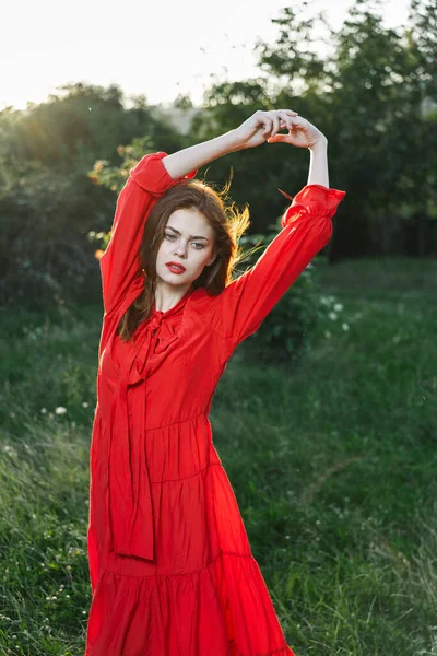 Приваблива жінка в червоній сукні позує в природі зеленою травою — стокове фото