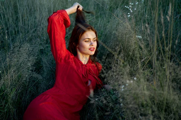 Pretty woman in red dress lies on the grass nature sun — Stock Photo, Image