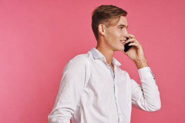 Beyaz gömlekli yakışıklı adam telefonda pembe arka planda konuşuyor.