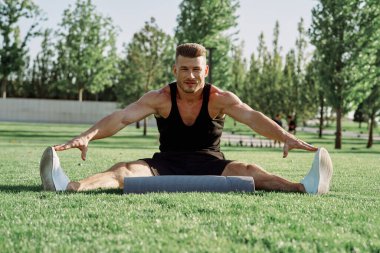 Sportif adam parkta çimlerde oturuyor.