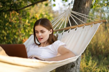 Kadınlar dışarıda bir hamakta dizüstü bilgisayarlı internetle yatıyor.