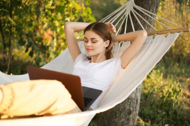 Kadınlar hamakta dizüstü bilgisayarlı tatil internetleriyle yatıyor.