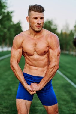 Şişirilmiş kaslı vücutlu bir adam dışarıda sağlık egzersizi yapıyor.