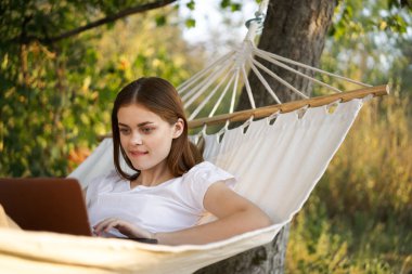 Kadınlar dışarıda bir hamakta dizüstü bilgisayarlı internetle yatıyor.