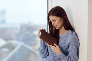 Kadın pencerenin yanında kitap okuyor, bir bardak içkiyle dinleniyor.