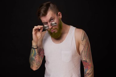 Kollarında dövme olan yakışıklı bir adam. Güneş gözlüğü takıyor. Geçmişi koyu renk.