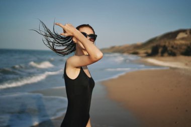 Siyah mayo giymiş bir kadın, kumlu sahilde yürüyor. Tropiklerde.