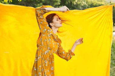 Sarı elbiseli gülümseyen kadın doğaya sarılık pozu veriyor.