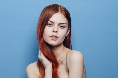 Çıplak omuzlu bir kadın. Kızıl saçlı, mavi arkaplan.