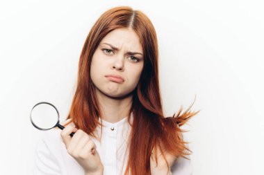 Ellerinde büyüteçle beyaz gömlekli kızıl saçlı bir kadın...