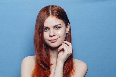 Çıplak omuzlu çekici bir kadın. Kızıl, yakın plan, mavi arka plan.