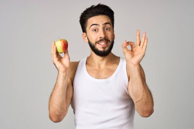 Beyaz tişörtlü bir adam taze meyve elmalı vitaminler izole edilmiş arka plan.