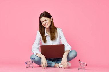 Dizüstü bilgisayarı olan bir kadın internet alışverişinde pembe arka planda oturuyor.