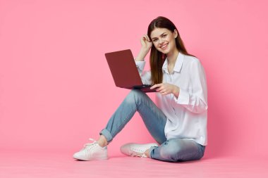 Pembe arka plan internet teknolojisinde dizüstü bilgisayarı olan neşeli bir kadın.