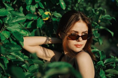 Güneş gözlüklü ve yeşil yapraklı neşeli moda kadın Rus yazı