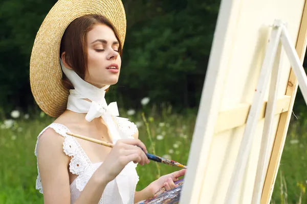 Csinos nő kalapos művész fest egy képet a természet festék — Stock Fotó
