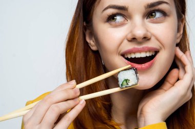 Japon yemek çubuklarıyla suşi yiyen kadın arka planda ışık yayıyor.