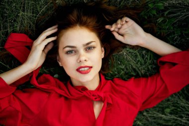 Kırmızı elbiseli kadın yaz aylarında çim adreste yatıyor.