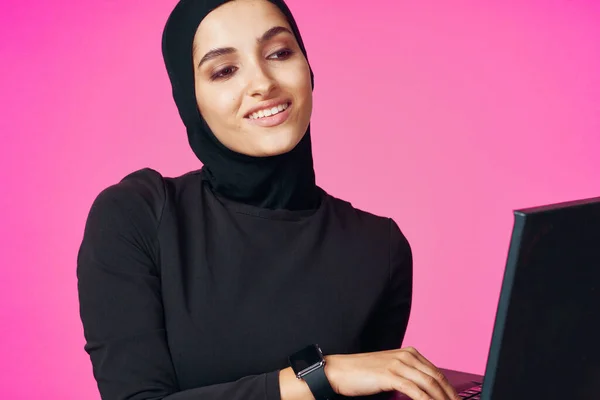 带头巾的穆斯林妇女，学习粉色背景的笔记本电脑技术 — 图库照片