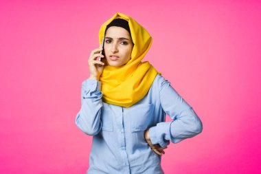 Sarı tesettürlü müslüman kadın telefon teknolojisi pembe arka planda konuşuyor.