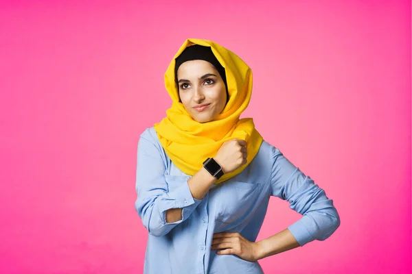 Wesoła kobieta w żółtym hijab elektroniczny zegarek technologia użytkownik różowy tło — Zdjęcie stockowe