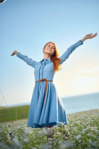 Kvinna i en blå klänning i ett fält i naturen hatt blommor gå — Stockfoto