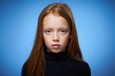 Yüzünde çilleri olan kızıl saçlı kız yakın plan mavi arka plan pozu veriyor.