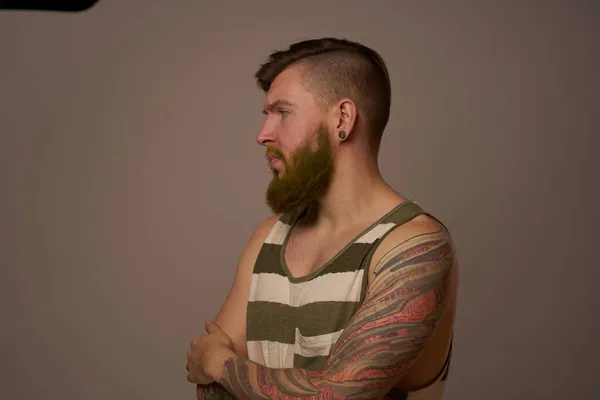 Brodaty mężczyzna w koszulce w paski z tatuażami pozujący studio — Zdjęcie stockowe
