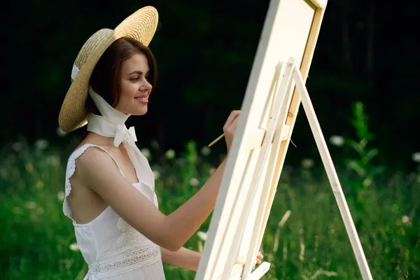 Mujer en vestido blanco pinta un cuadro sobre caballete de la naturaleza — Foto de Stock