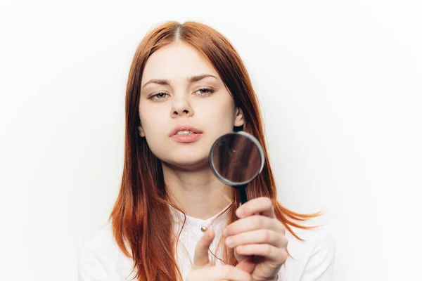 Femme aux cheveux roux dans une chemise blanche avec une loupe dans ses mains à la recherche — Photo