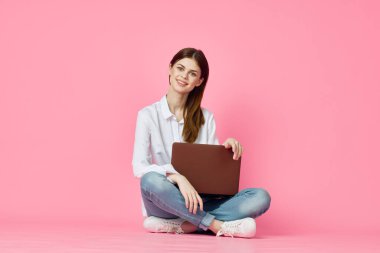 Dizüstü bilgisayarı olan bir kadın internet alışverişinde pembe arka planda oturuyor.