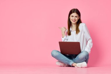 Dizüstü bilgisayar alışverişi yapan pembe arka planda oturan bir kadın.