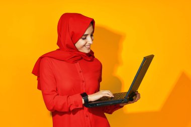Elinde dizüstü bilgisayarla kırmızı tesettürlü kadın. Teknoloji, duygu, etnik model.