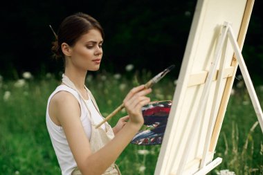 Neşeli kadın ressam açık havada yaratıcı bir resim çiziyor.