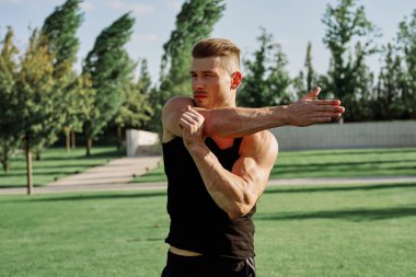 Siyah tişörtlü bir adam, doğa parkında dambıl egzersizi yapıyor.