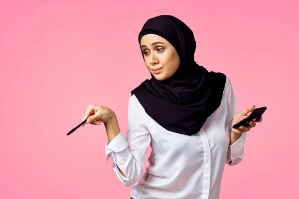 計算機とお金のピンクの背景を持つイスラム教徒の女性 — ストック写真