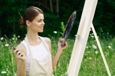 Neşeli kadın bir palet doğa resmi çiziyor.