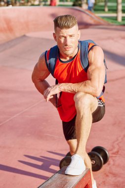 Parkın içinde elinde dambıllar olan atletik bir adam.