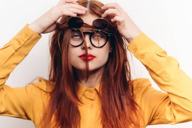 Kırmızı saçlı, güneş gözlüğü takan, moda arkaplanı pozu veren bir kadın.