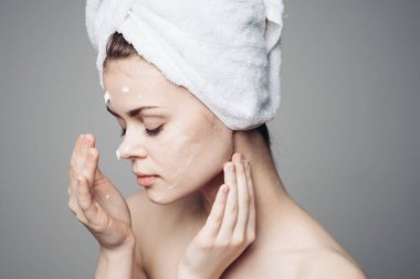 Çıplak omuzlu kadın yüz kremi sürmüş.