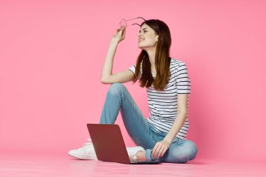 Dizüstü bilgisayarı olan bir kadın internet iletişiminde pembe arka planda oturuyor.