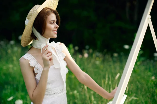 Femme en robe blanche peint un tableau sur chevalet de la nature — Photo