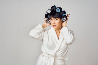 Kafasında bigudileri olan beyaz cüppeli bir kadın mutfakta ödev yapıyor.