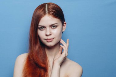 Çıplak omuzlu bir kadın. Kızıl saçlı, mavi arkaplan.