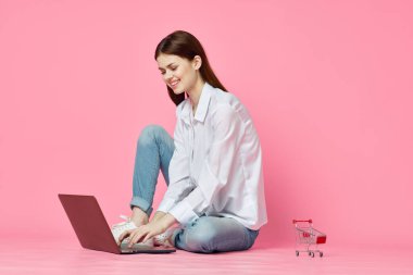 Pembe arka planda dizüstü bilgisayarı olan neşeli bir kadın.
